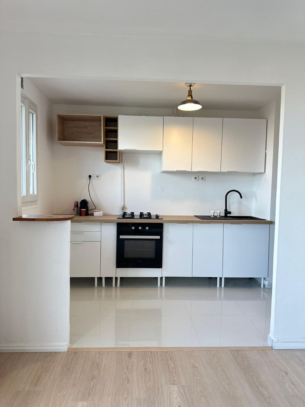 Cuisine blanche ouverte avec plan de travail bois, four encastré, plaque de cuisson et étagères
