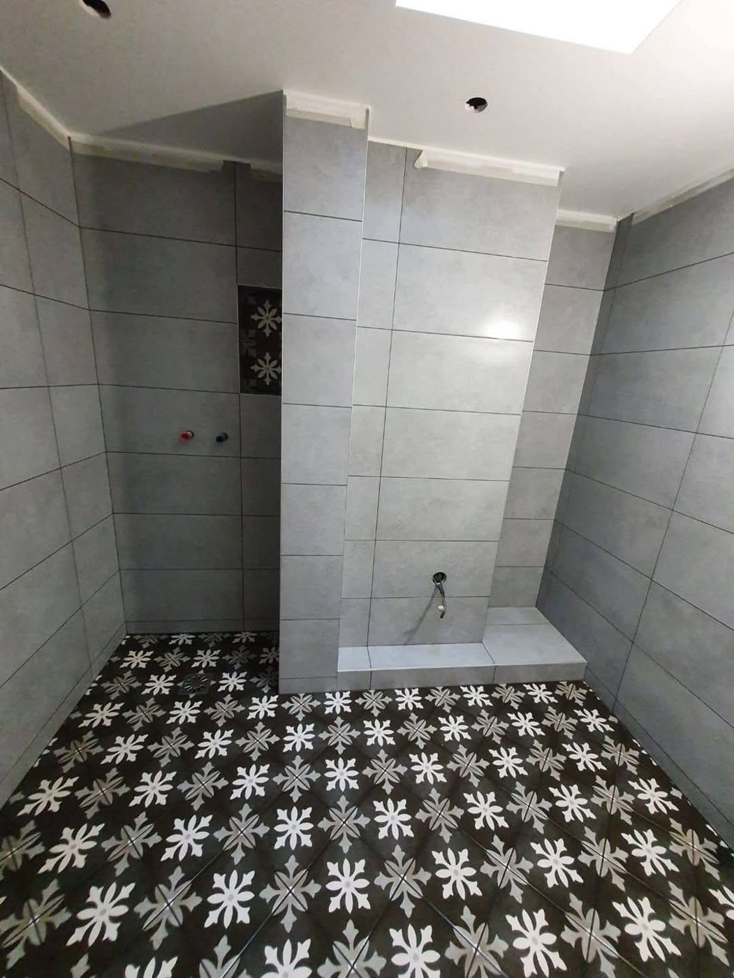 Salle de bain en cours de rénovation avec carrelage mural gris et sol à motifs floraux noir et blanc