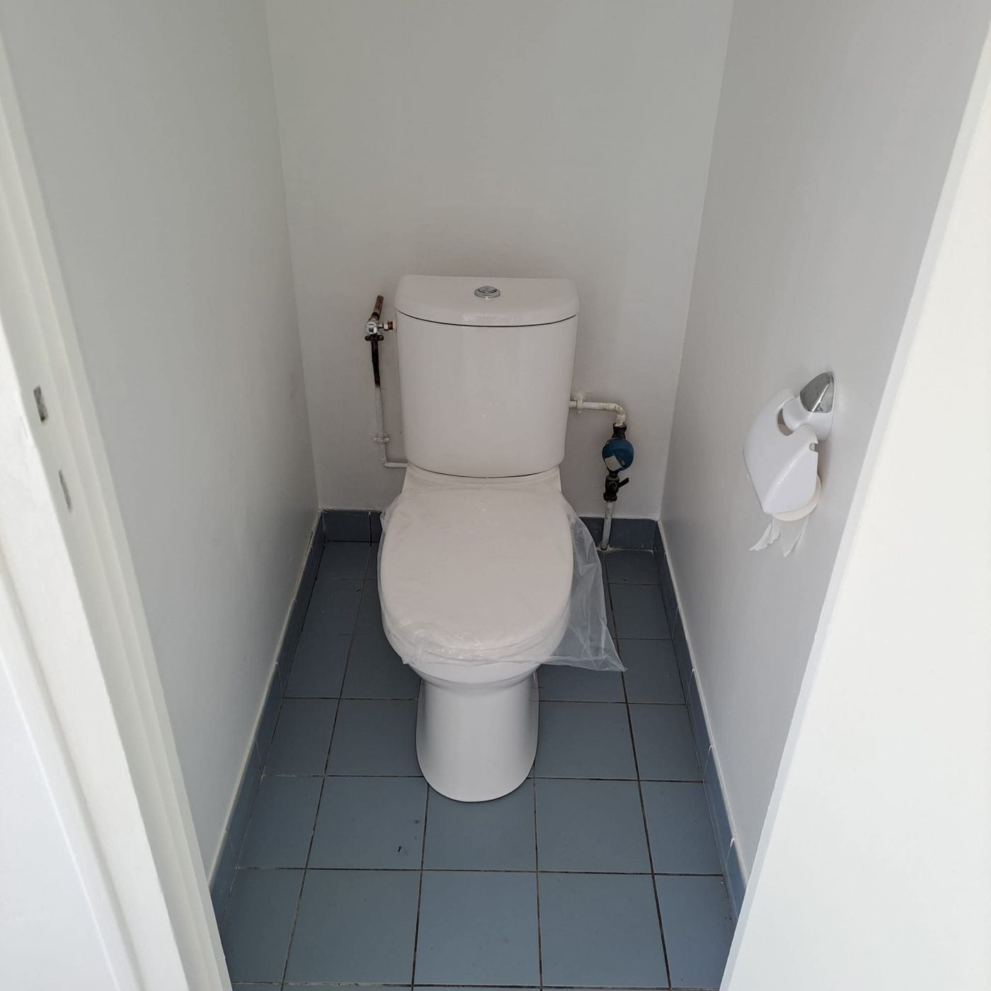 Toilettes rénovées avec carrelage bleu au sol et murs blancs