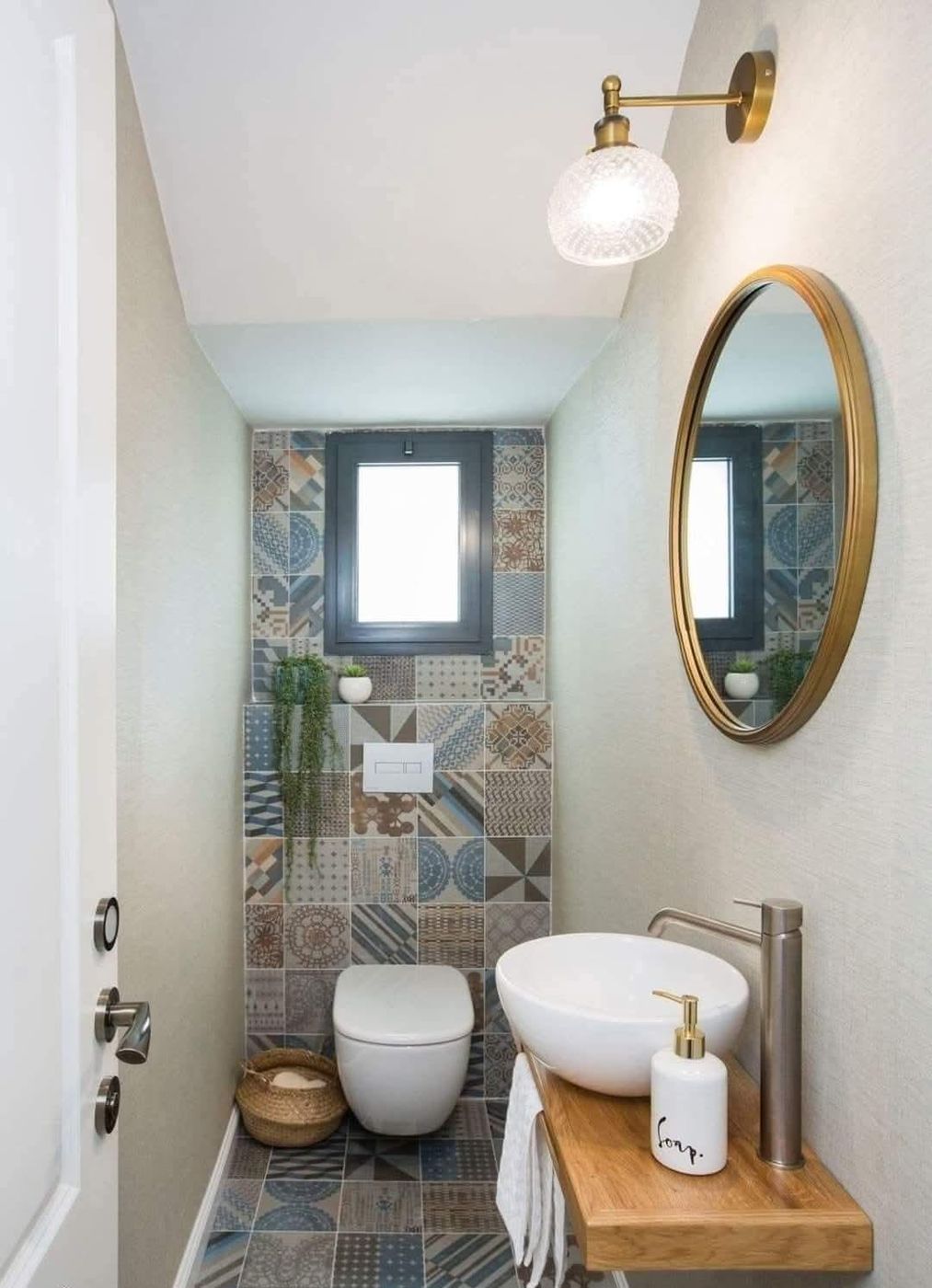Toilettes avec WC suspendu, carreaux de ciment colorés, lave-mains sur plan en bois et miroir doré